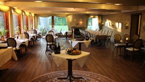 A restaurant with multiple tables and chairs, a fireplace, and a view of the outdoors. - Bov Kro (Padborg)