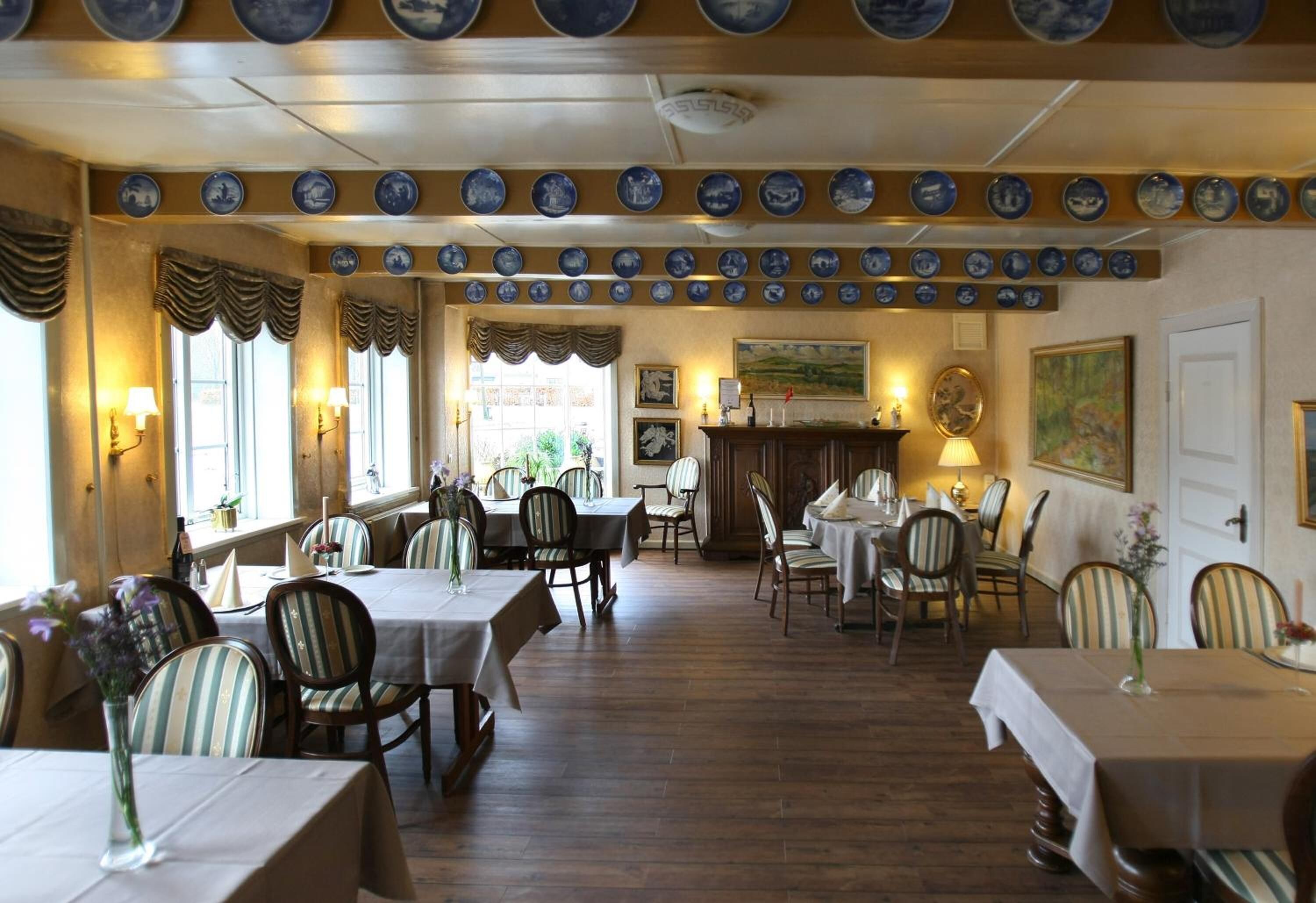 Un espace repas comprenant plusieurs tables et chaises, un plafond orné de motifs et des assiettes décoratives accrochées au mur.
