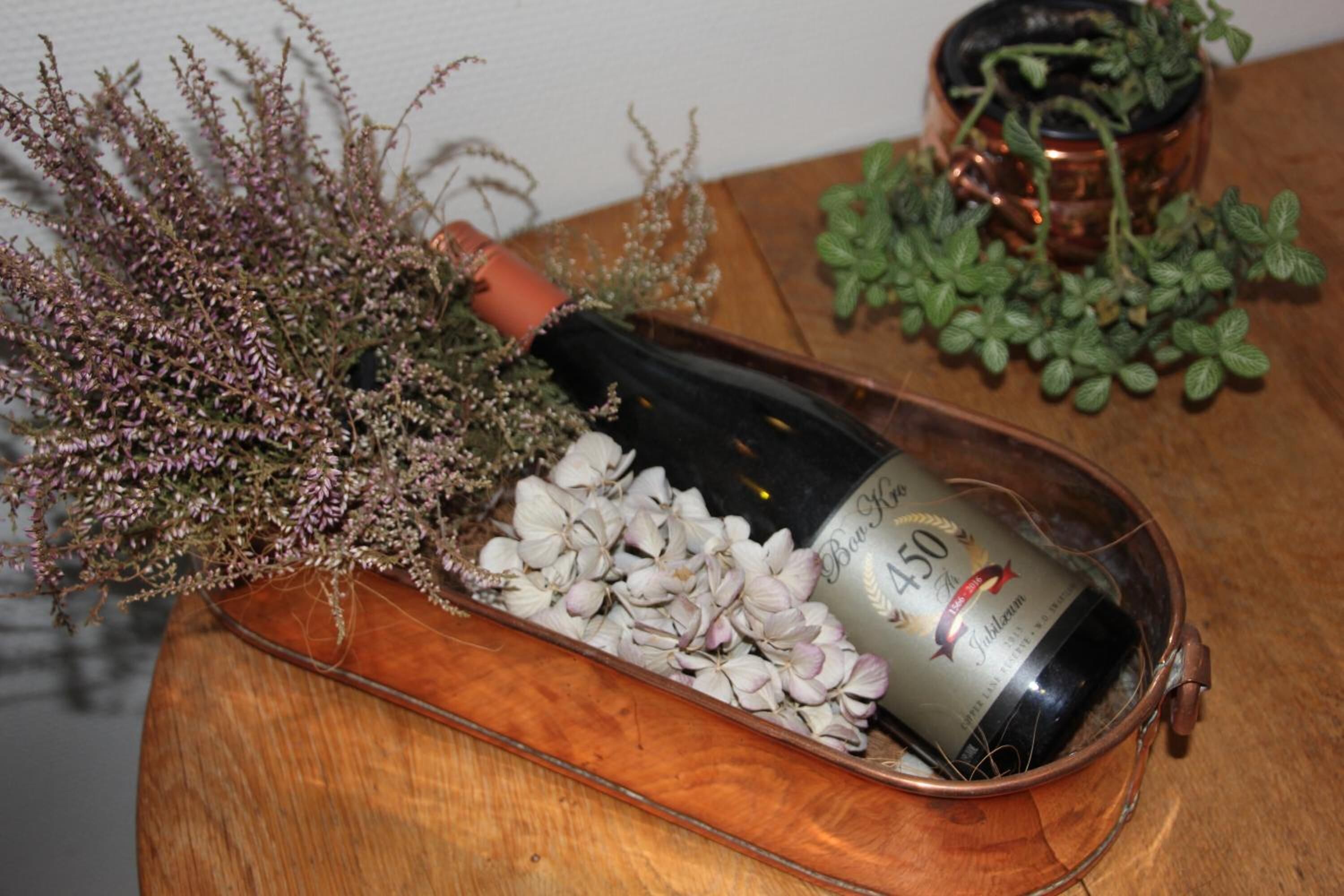 A bottle of wine in a copper decanter on a wooden tray.
