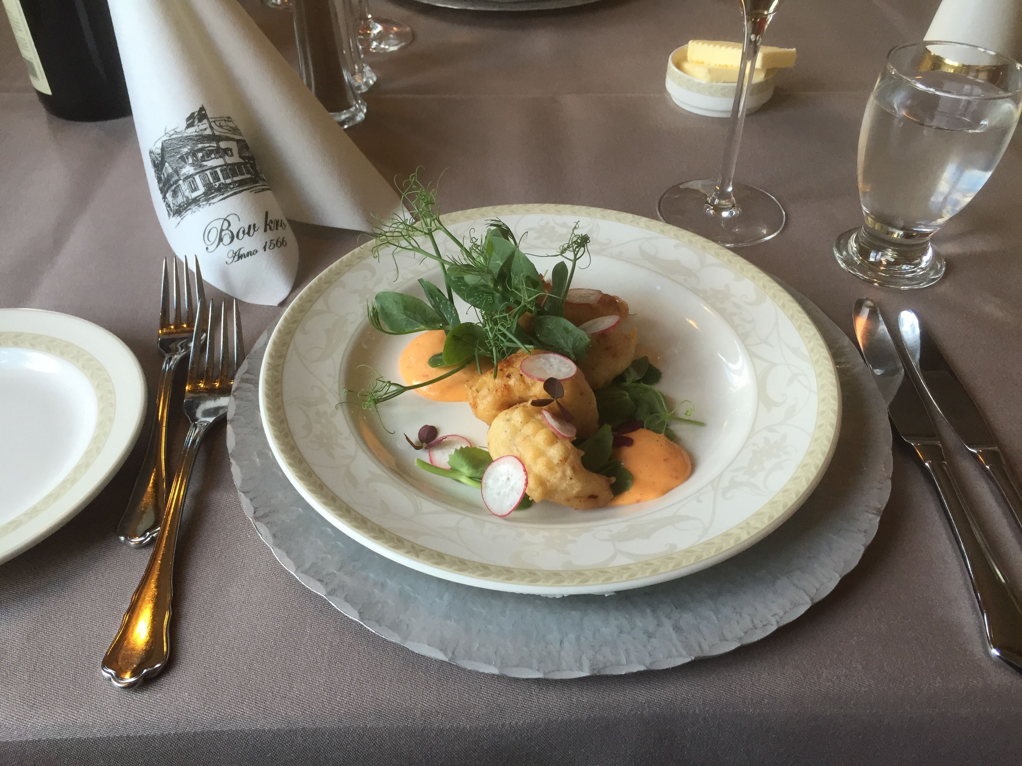 Une table dressée pour un repas formel, avec une assiette de nourriture, des couverts et un verre d’eau.