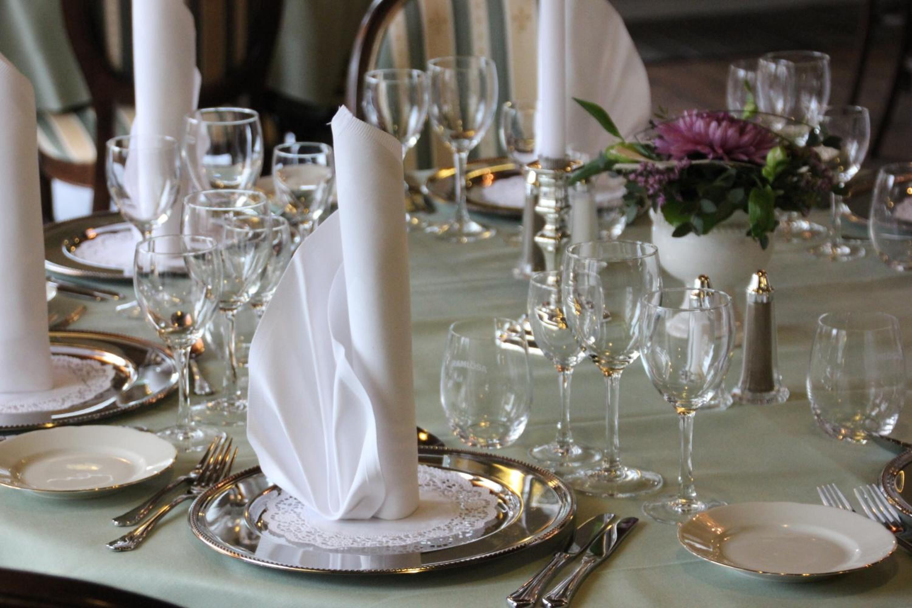 Ein Tisch ist für ein festliches Essen gedeckt, mit weißen Servietten, Besteck und klarem Glas.