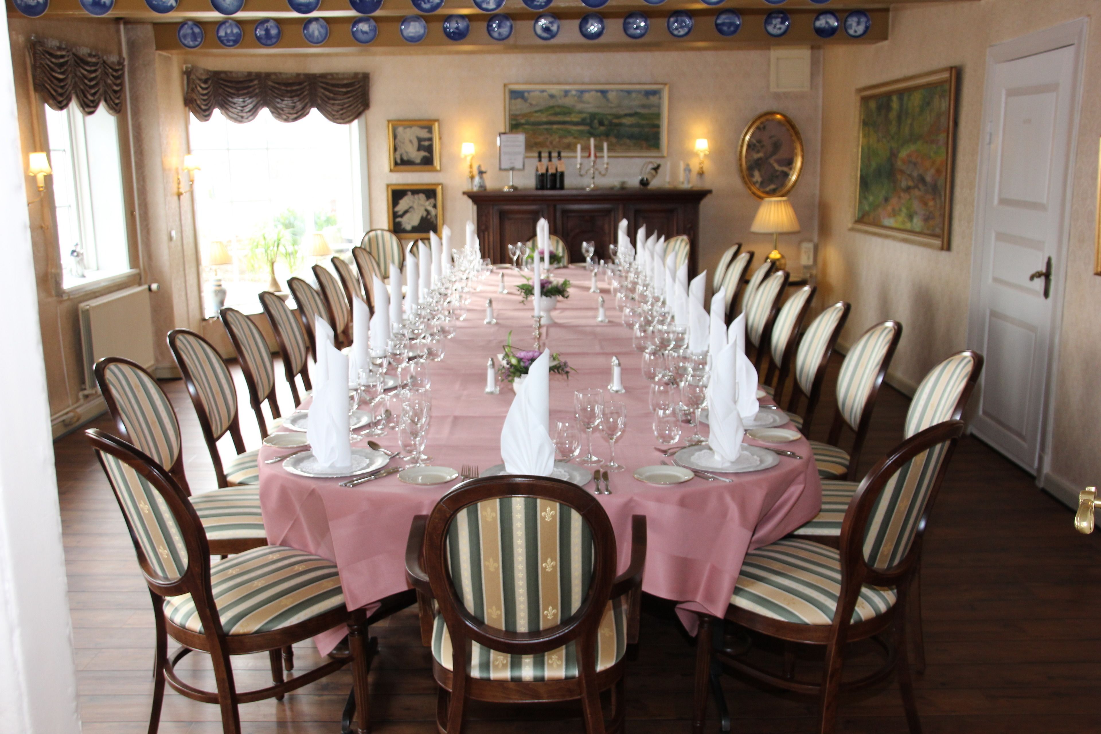 A formal dining room with a long table set for a meal, surrounded by chairs with striped upholstery.