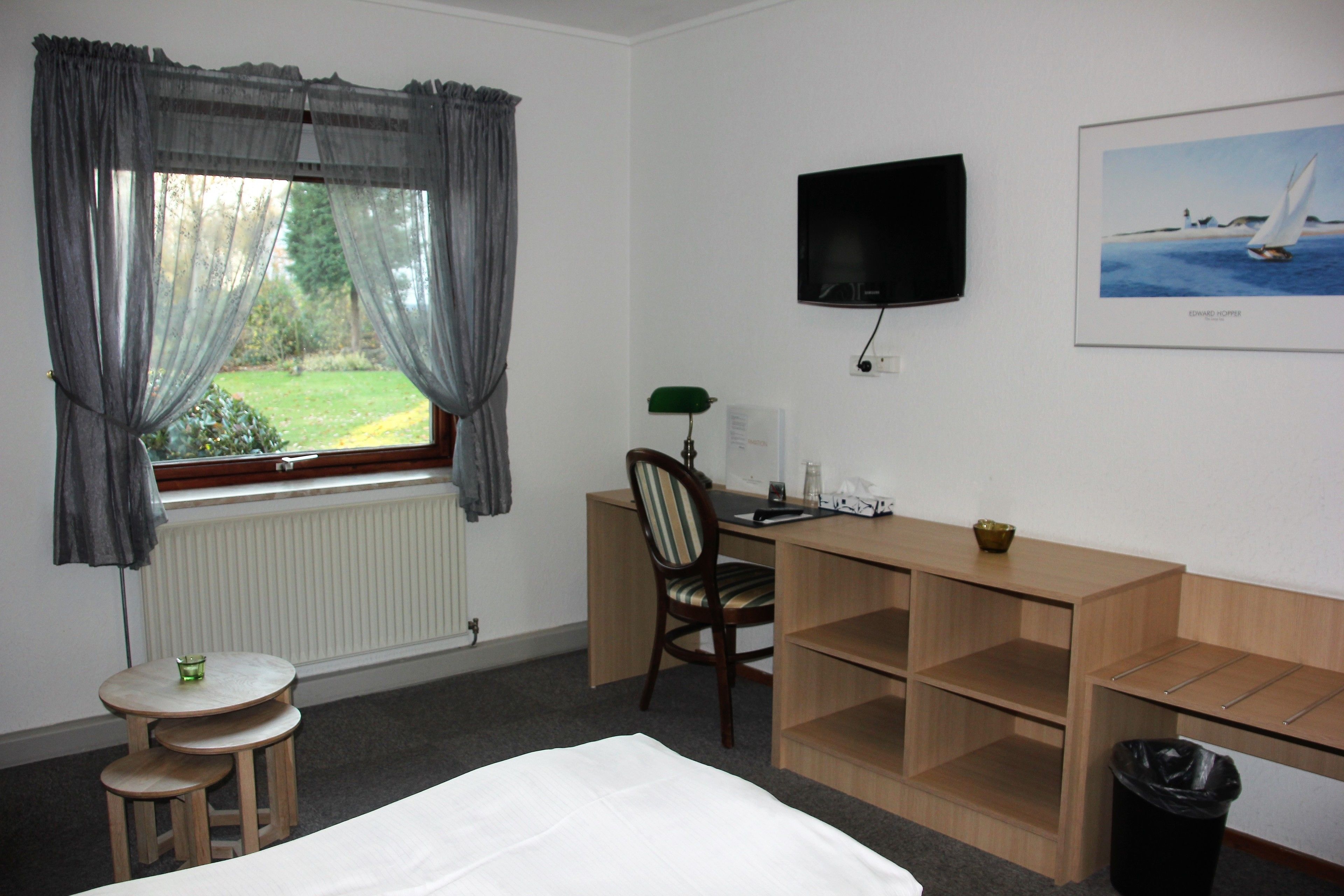 A hotel room with a bed, a desk, a chair, a TV, a window with curtains, and a picture on the wall.