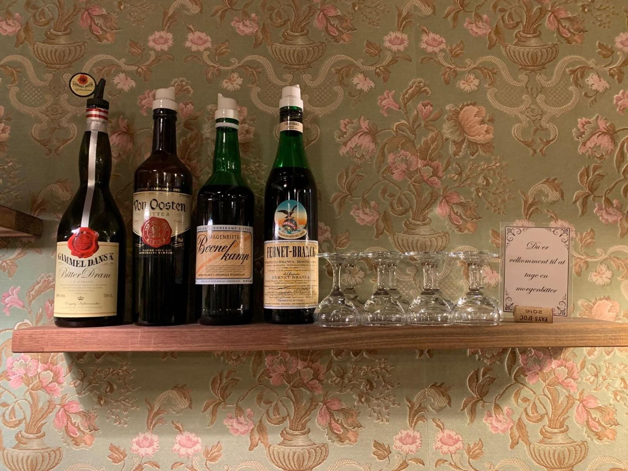 A shelf with four bottles of wine and several wine glasses.