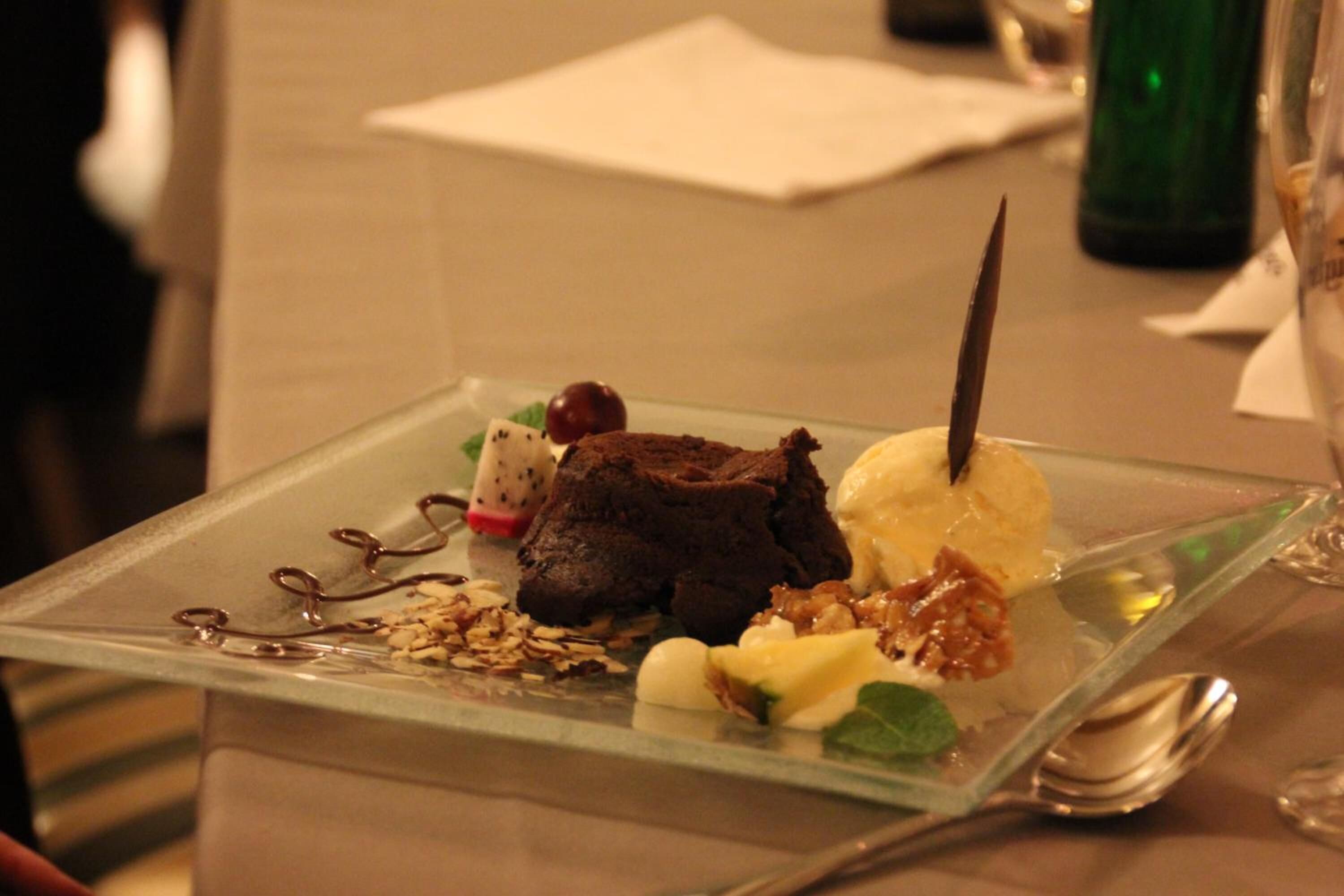 Ein Dessertteller mit Schokoladendessert, Eis und Nüssen auf einer klaren Glasschale.