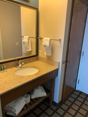 A bathroom with a granite countertop sink, a mirror, a towel rack, and a door. - Baymont by Wyndham San Angelo (San Angelo)