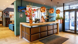 A reception desk with a modern design, a large clock, and a view of the street outside. - Roombach Hotel Budapest Center (Budapest)