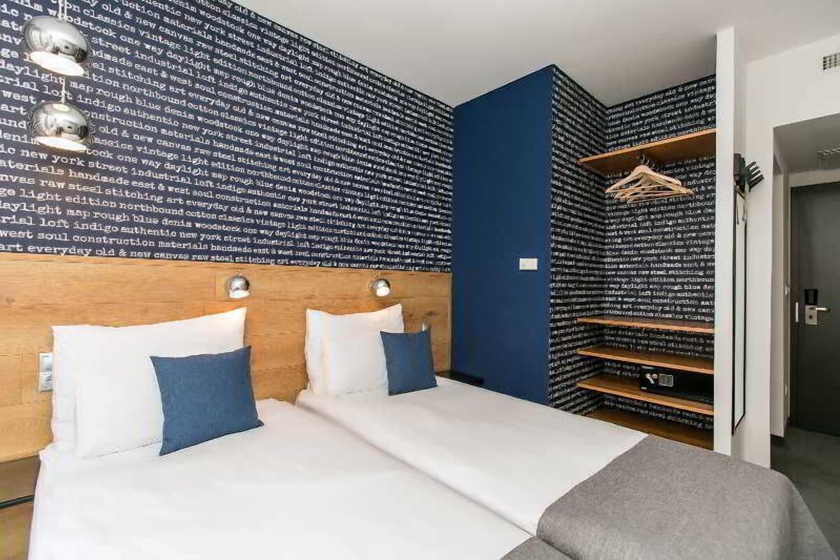 A hotel room with a bed, two bedside tables, a wardrobe, and a wall with text.