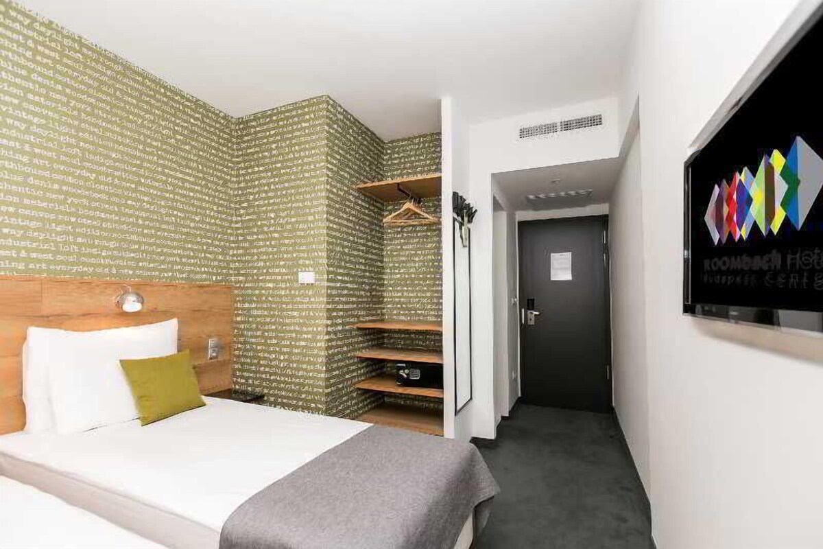 A hotel room with a bed, a wardrobe, and a door leading to a hallway.