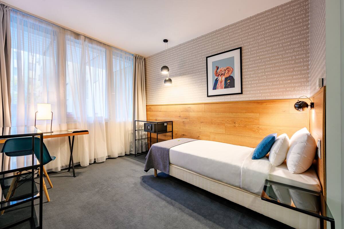 A hotel room with a bed, a desk, a chair, and a large window with curtains.