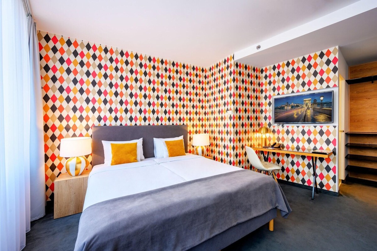 A hotel room with a bed, bedside tables, a desk, and a TV.