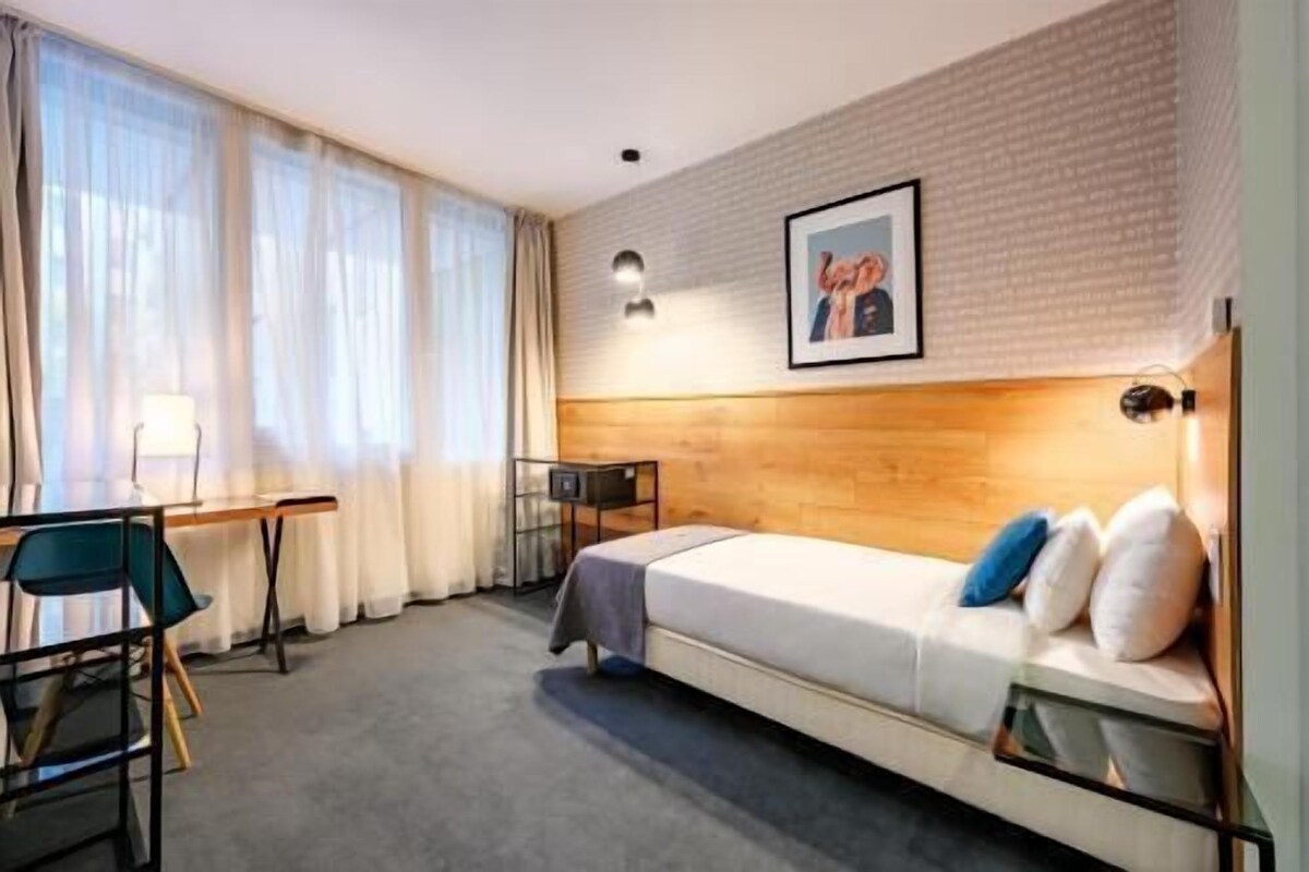 A hotel room with a bed, a desk, a chair, and a window with curtains.