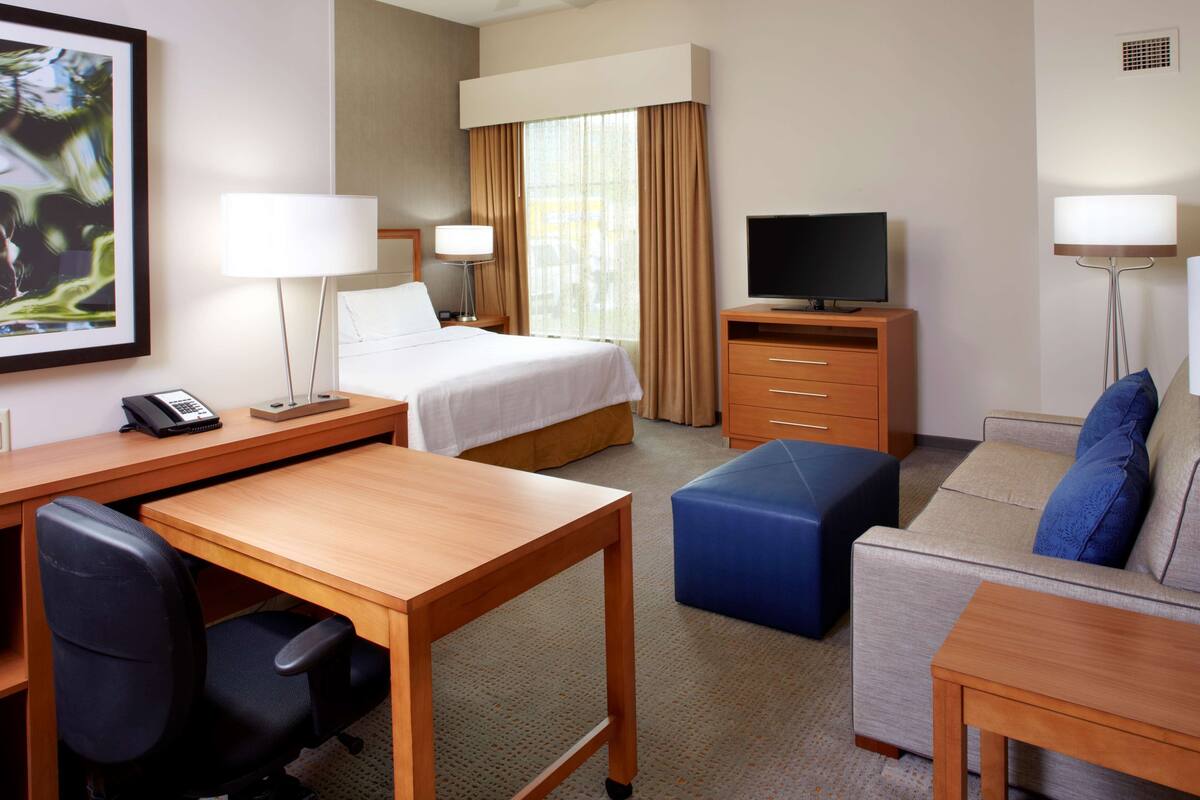 Una habitación de hotel con cama, escritorio, silla, televisor, sofá y lámparas.