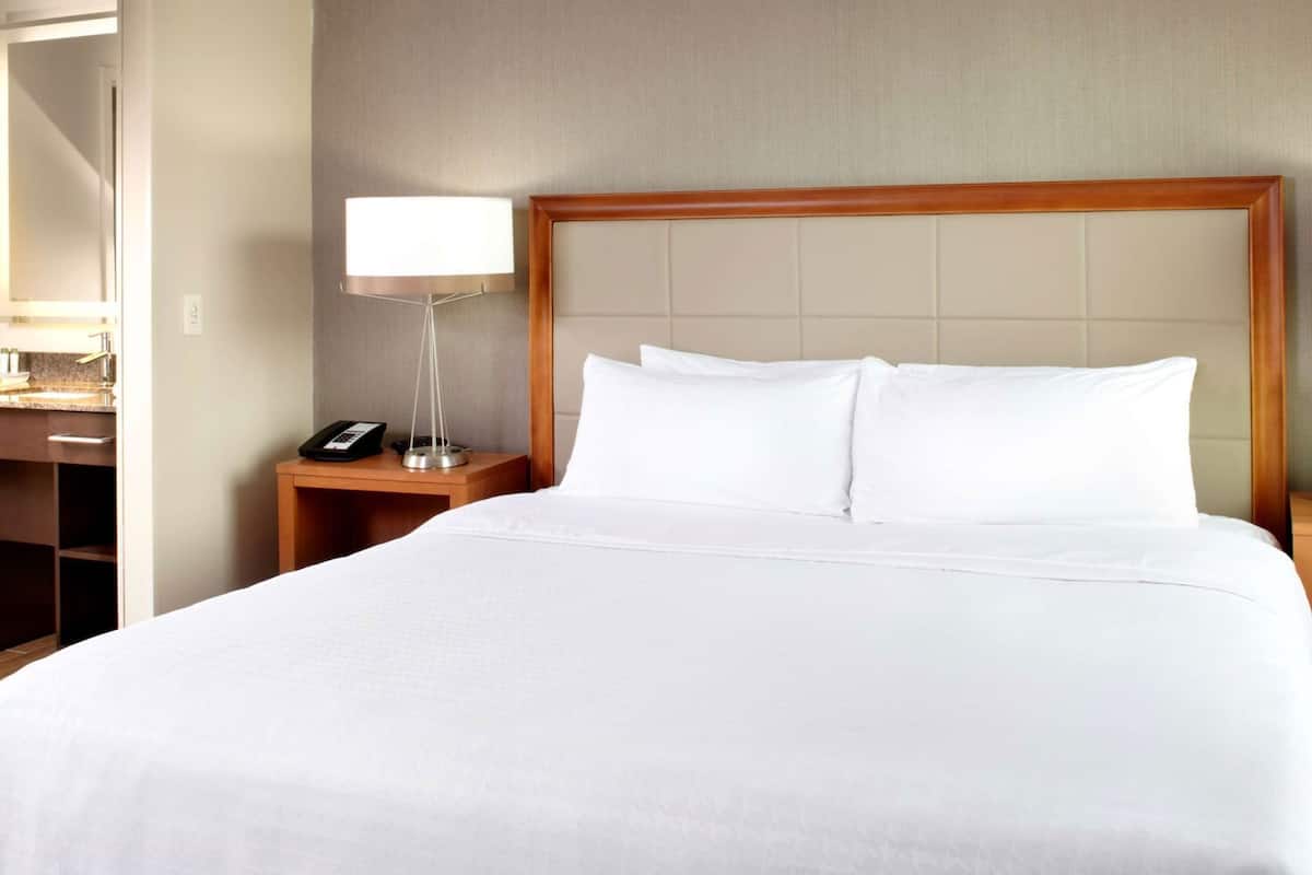 Habitación de hotel con una cama grande, una lámpara de noche, una mesita de noche con teléfono y un escritorio con espejo.