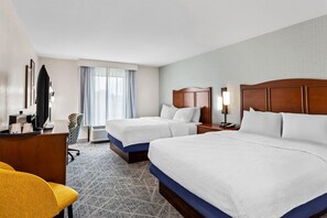 A hotel room with two beds, a desk, a chair, and a window with curtains.