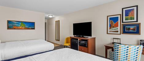 A hotel room with two beds, a television, a microwave, and artwork on the walls.