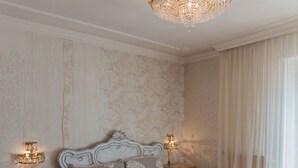A bedroom with a large ornate bed, two bedside tables with lamps, and a chandelier. - Hotel Corona Grossa (Balangero)