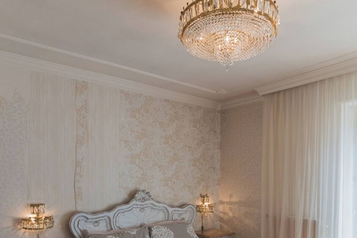 A bedroom with a large ornate bed, two bedside tables with lamps, and a chandelier.