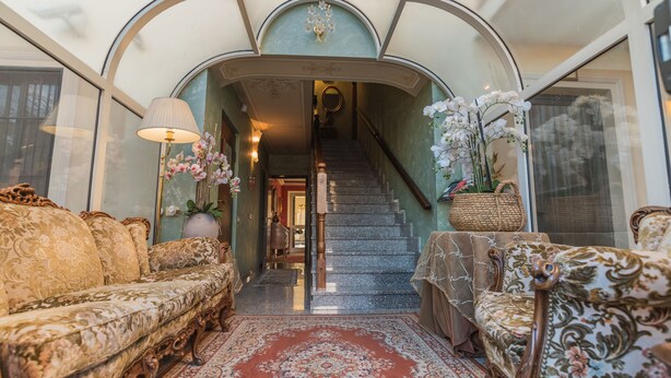 A grand staircase leading to a second floor, flanked by ornate sofas and a patterned rug. - Hotel Corona Grossa (Balangero)