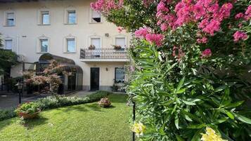 Un edificio con un giardino antistante, un balcone con ringhiera e una porta.