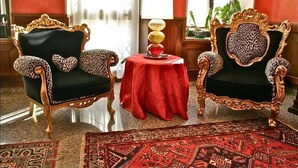 Two ornate chairs with leopard print upholstery, a red table with a decorative lamp, and a patterned rug in a well-lit room with red walls. - Hotel Corona Grossa (Balangero)