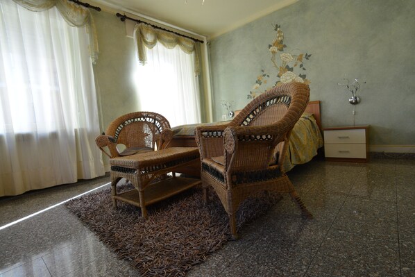 A room with two wicker chairs, a bed with a floral-patterned bedspread, a nightstand, and a wall-mounted vase. - Hotel Corona Grossa (Balangero)