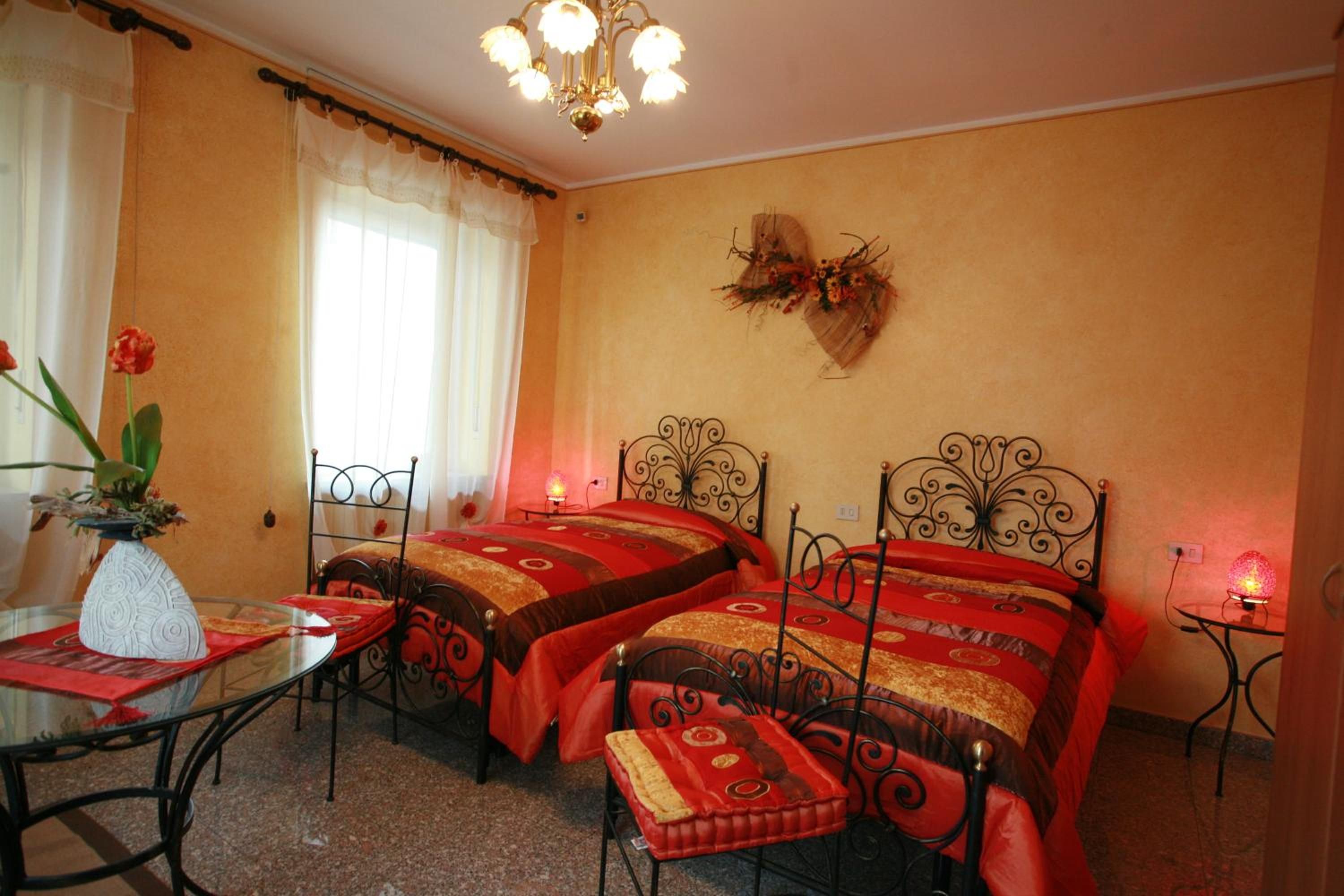 Una habitación de hotel con dos camas, un candelabro, una mesa con un florero y una ventana con cortinas.