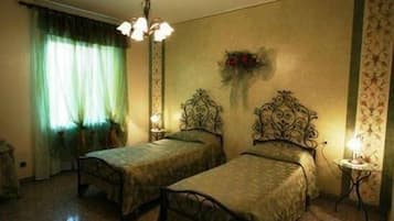 A room with two single beds, a chandelier, a vase with flowers on the wall, and a patterned wallpaper.
