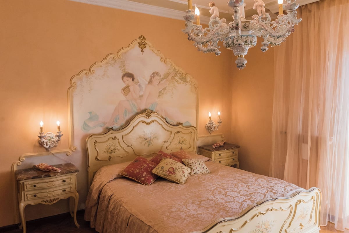 A bedroom with a large ornate bed, a chandelier, and a painting on the wall.
