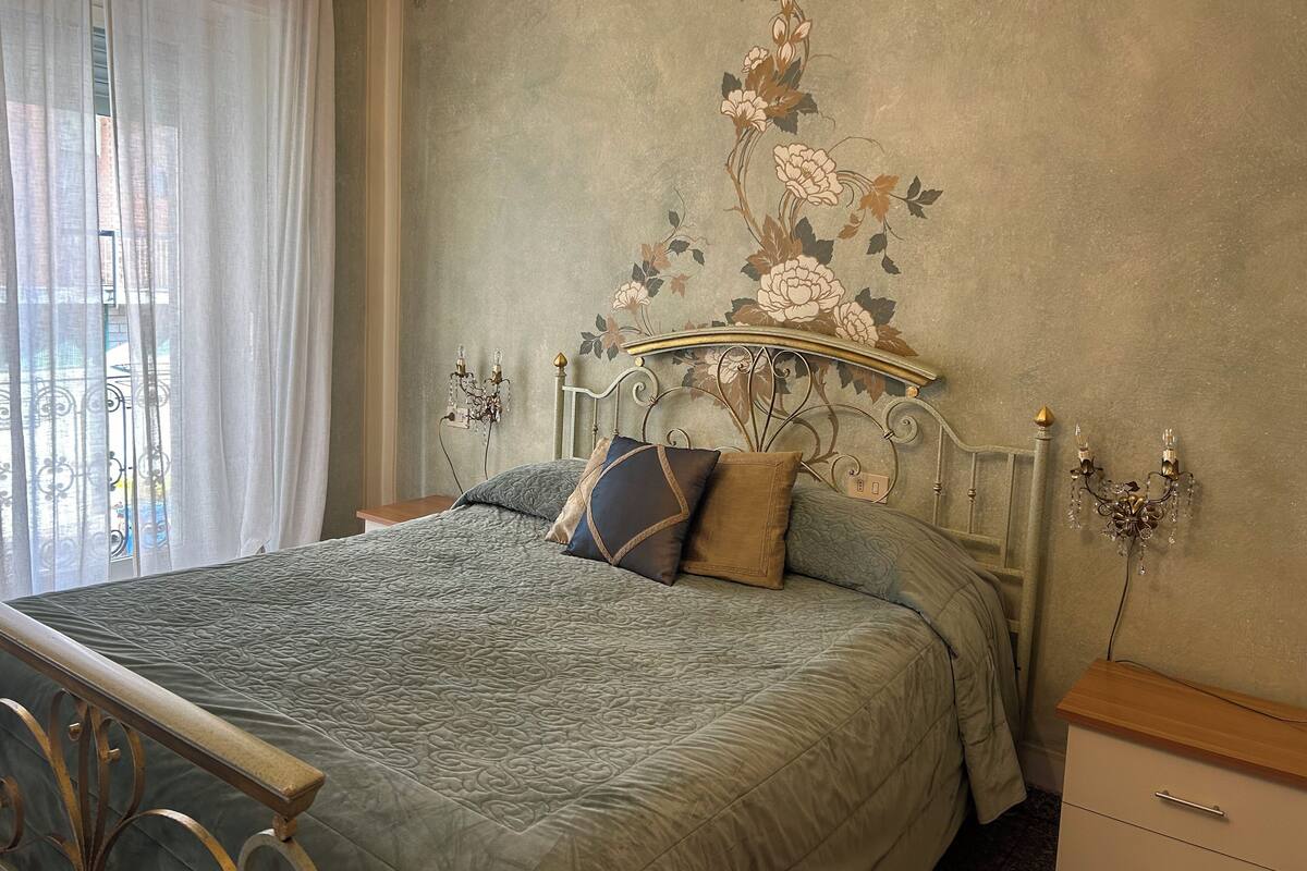 A bedroom with a large bed, a nightstand, a dresser, and a wall with floral wallpaper.