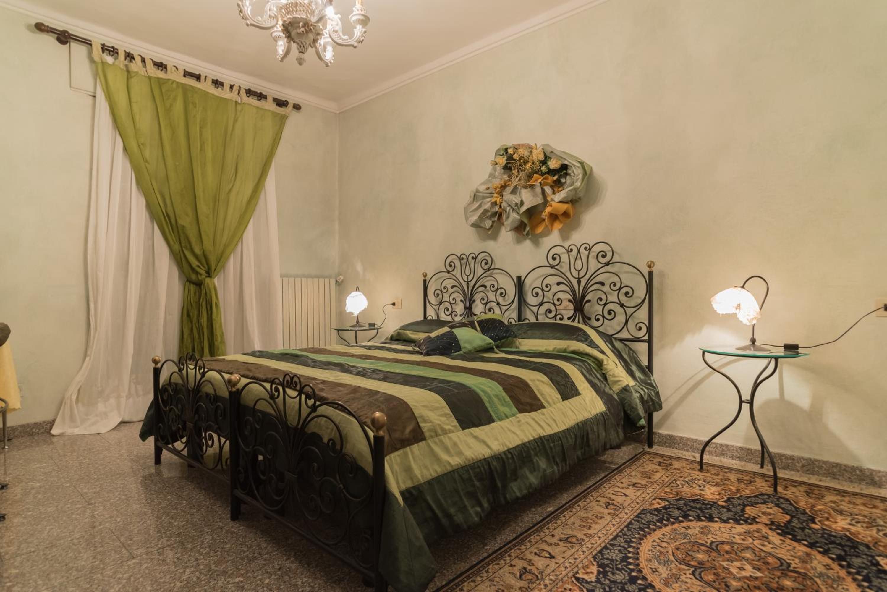 A bedroom with a bed, a chandelier, a table with a lamp, and a decorative wall piece.