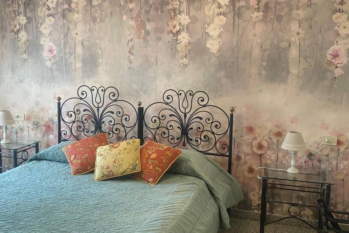 A bedroom with a bed, floral wallpaper, and two bedside tables with lamps.