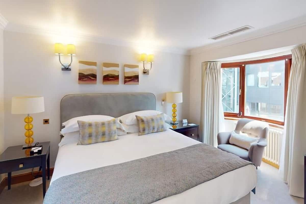 A hotel room with a large bed, two bedside tables with lamps, a chair, and artwork on the wall.