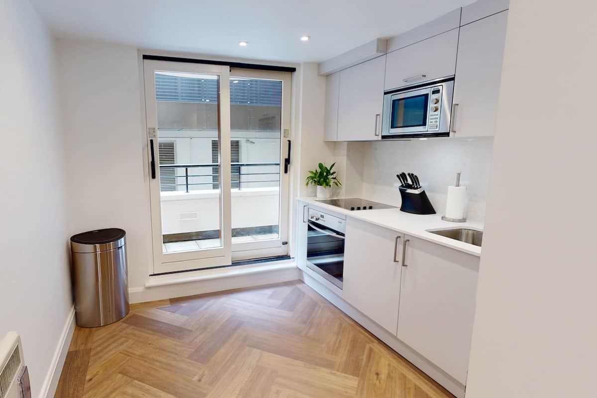 A modern kitchen with white cabinets, a stainless steel trash bin, a microwave, and a sink.