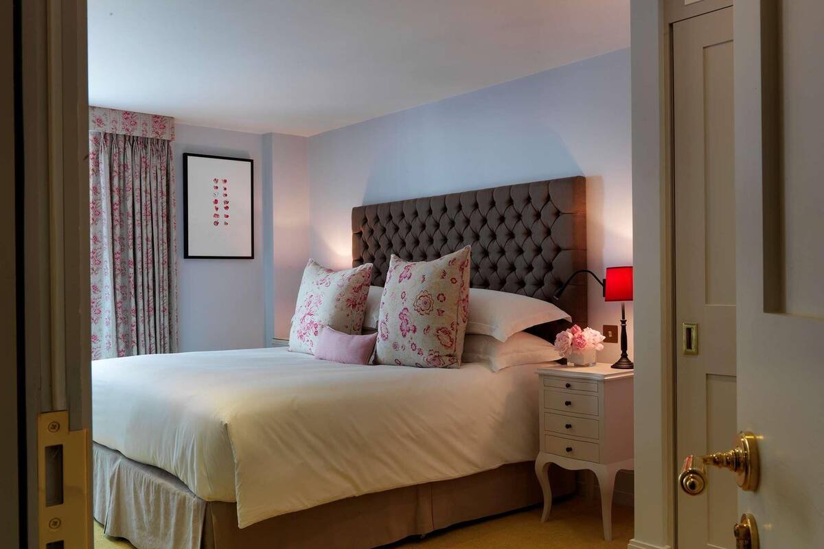 A bedroom with a large bed, a nightstand with a lamp, and a door with a brass handle.