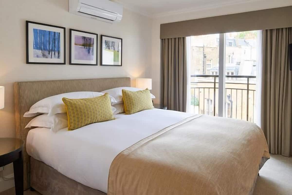 A hotel room with a large bed, two pillows, a nightstand, a lamp, and a window with curtains.