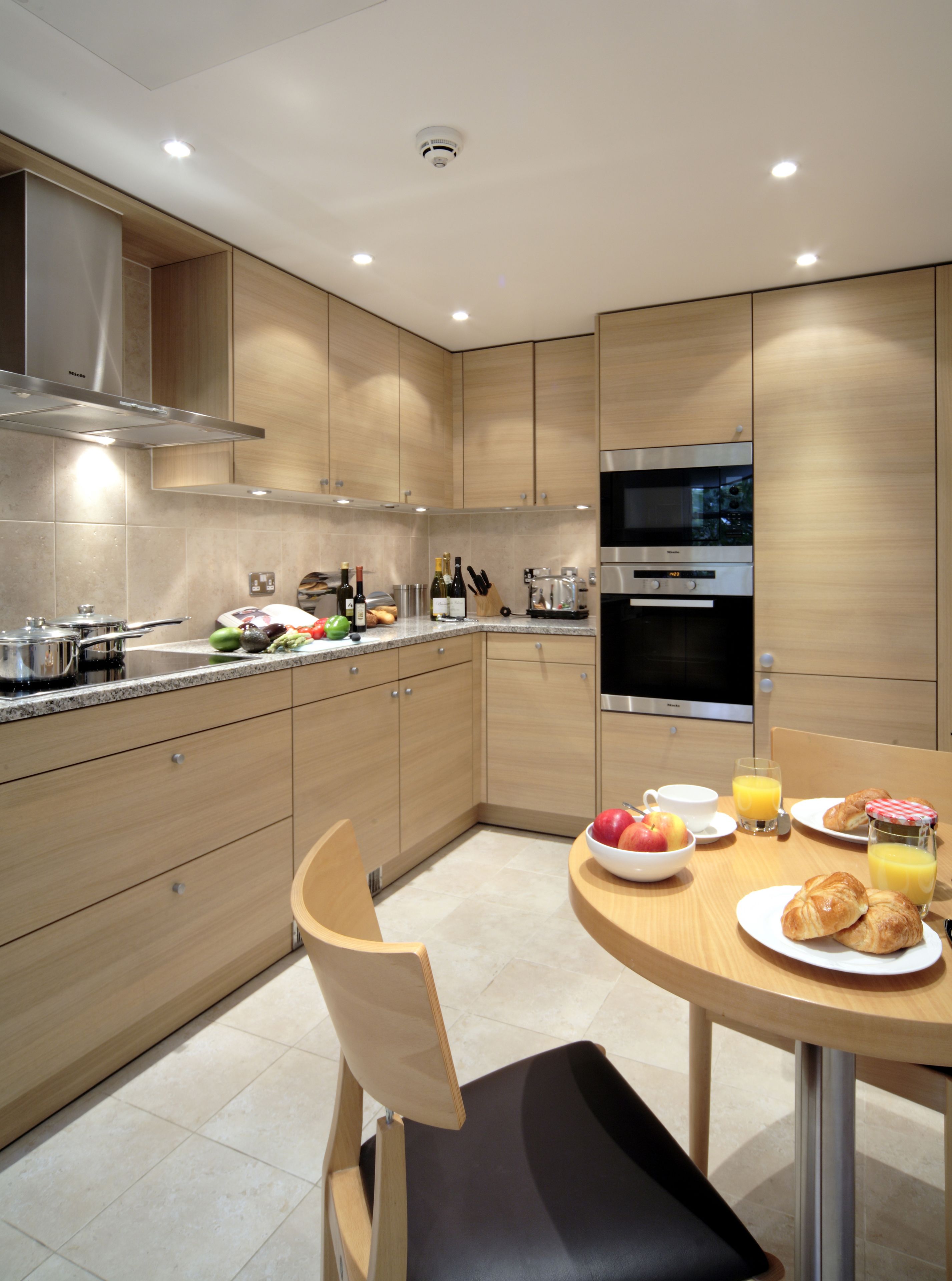 Een moderne keuken met houten kastjes, roestvrijstalen apparatuur en een ontbijtje op tafel.