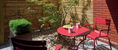 A patio with a wooden fence, a small garden, and a table with red chairs.