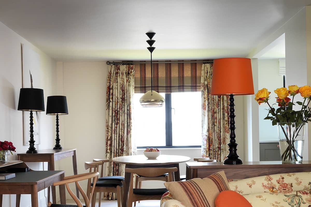 A living room with floral upholstery, a dining area with a table and chairs, and a window with curtains.
