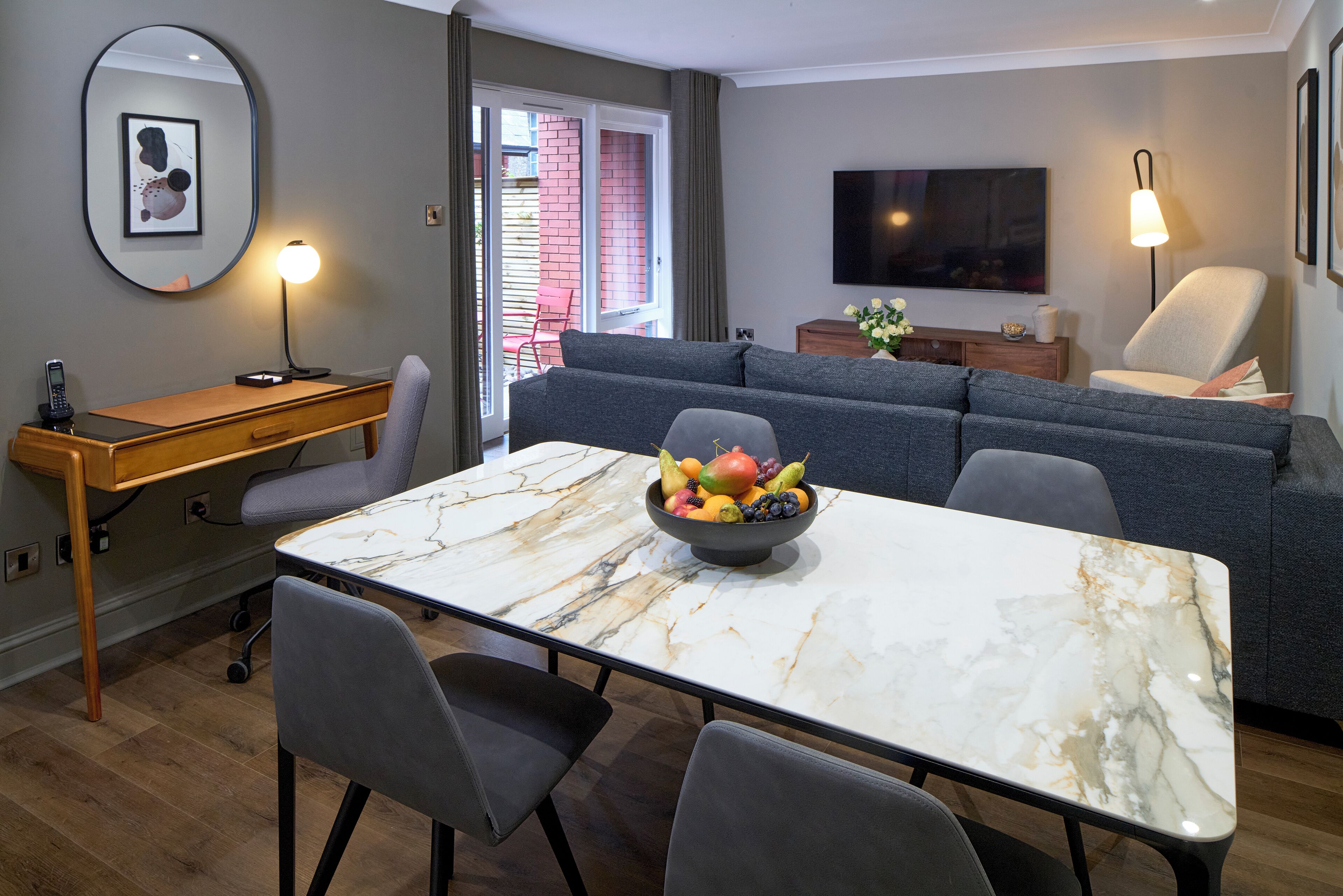 A modern living room with a marble table, grey sofa, and a fruit bowl.