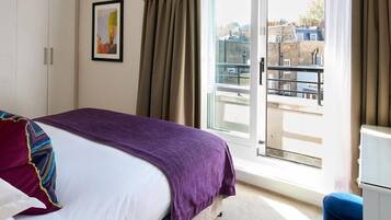 Quarto de hotel com cama, janela com cortinas, porta e vista para edifícios.
