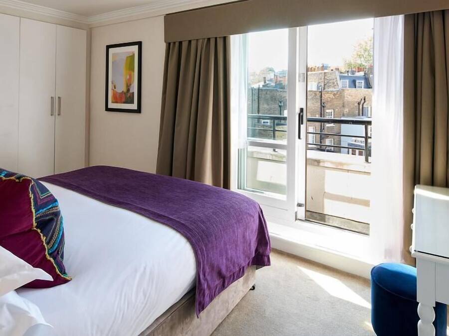 Quarto de hotel com cama, janela com cortinas, porta e vista para edifícios.