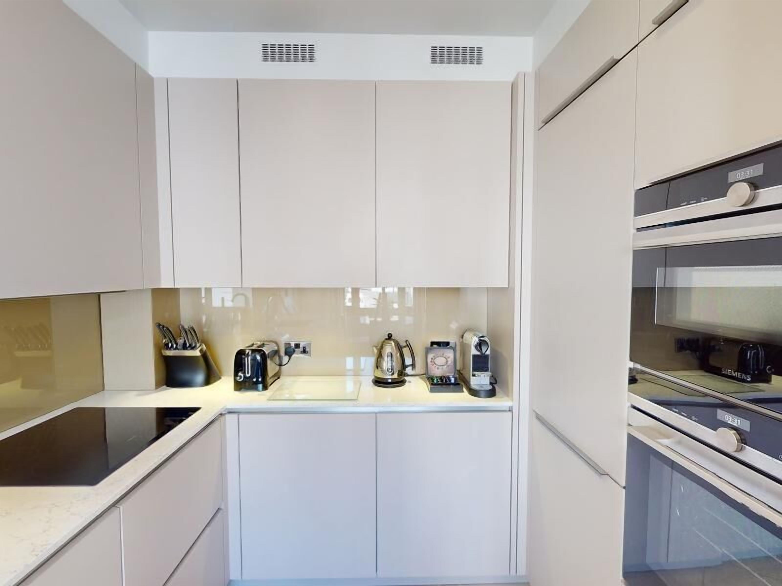Una cocina moderna con muebles blancos, encimera negra y horno Siemens.