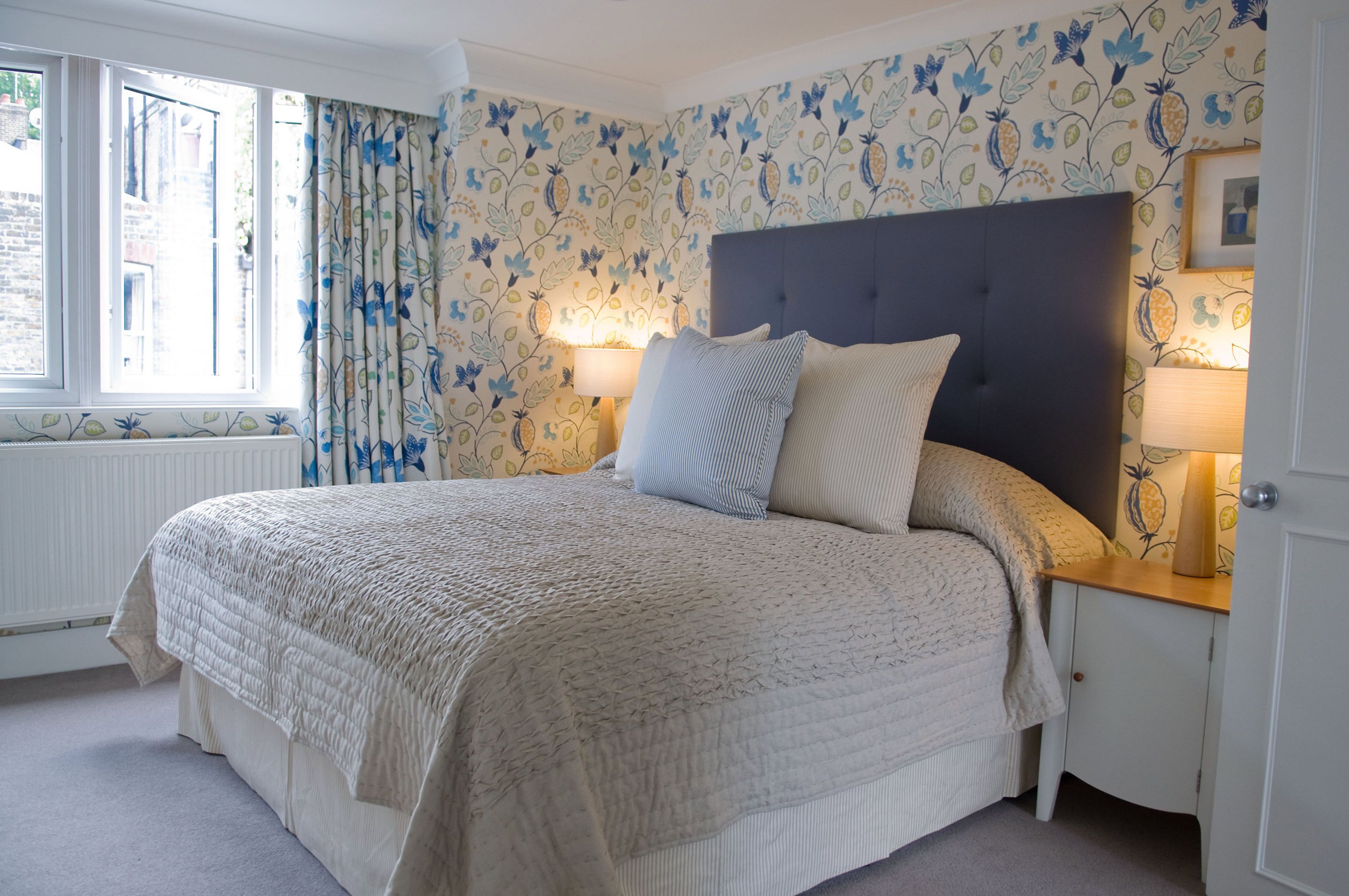 Une chambre à coucher avec un grand lit, un papier peint à motifs floraux et deux lampes de chevet.