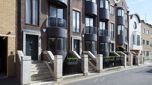 Une rangée de maisons de ville modernes, avec des balcons noirs, des façades en briques et un ciel d’un bleu éclatant.