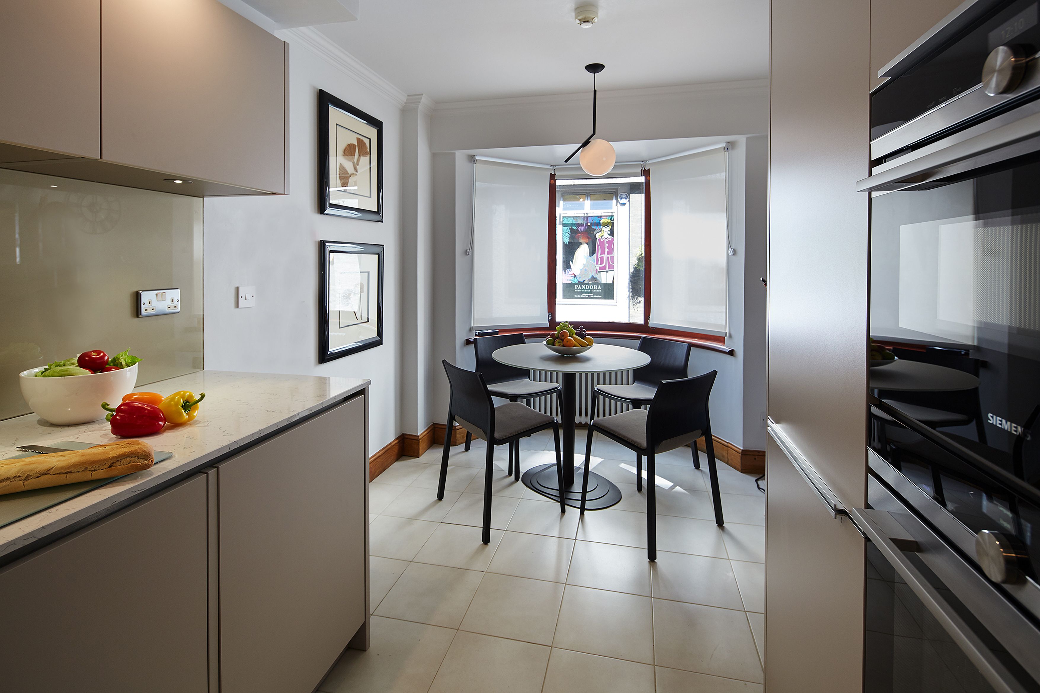 Une cuisine moderne avec un coin repas, comprenant une table ronde et des chaises, un four encastré et une fenêtre offrant une vue agréable.