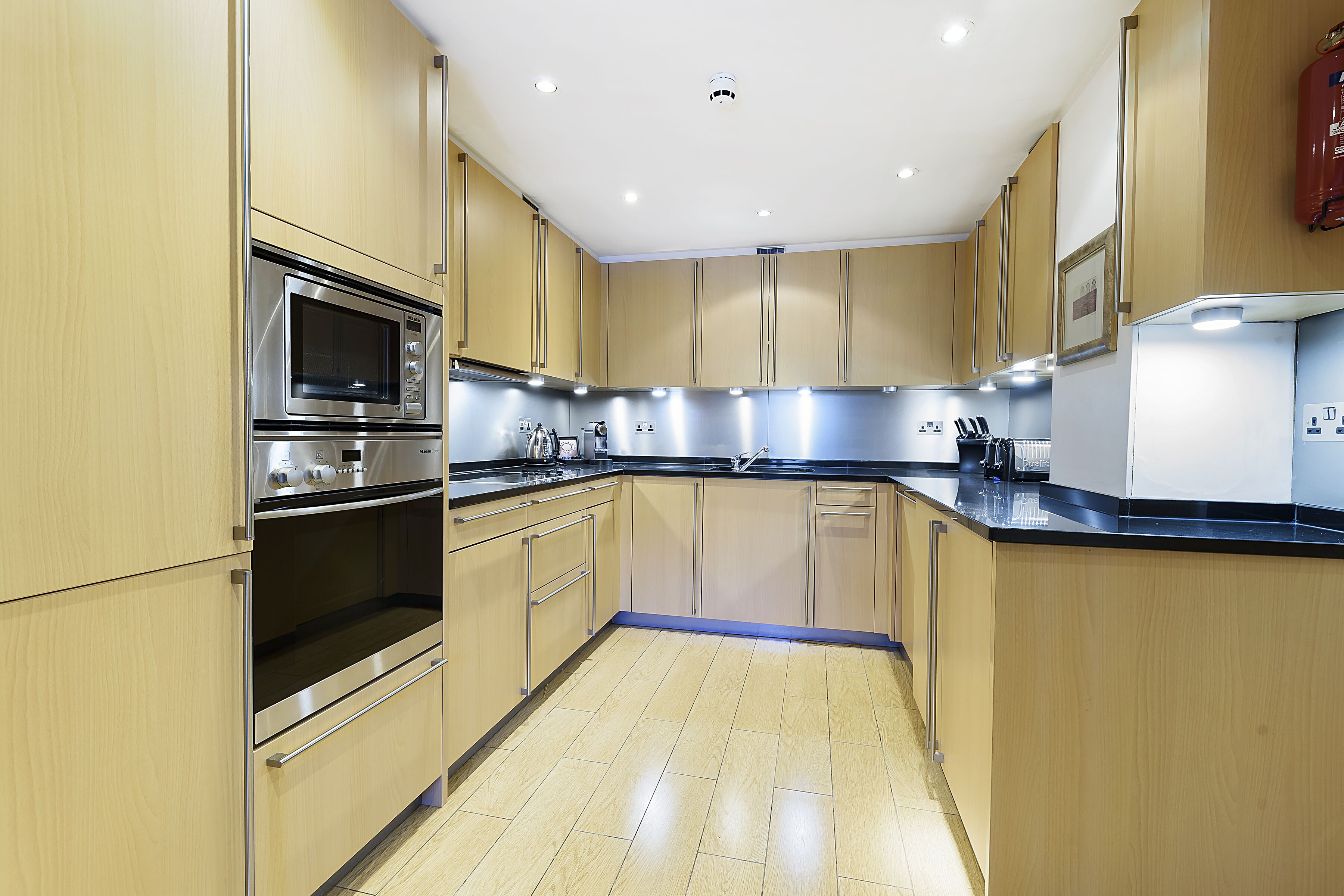 Une cuisine moderne avec des meubles en bois, des appareils électroménagers en acier inoxydable et un plan de travail noir.