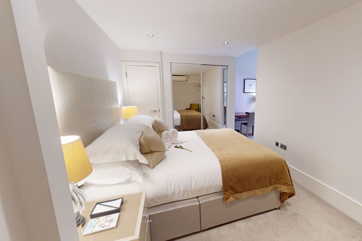 A hotel room with a bed, bedside table, lamp, and a desk with a chair.