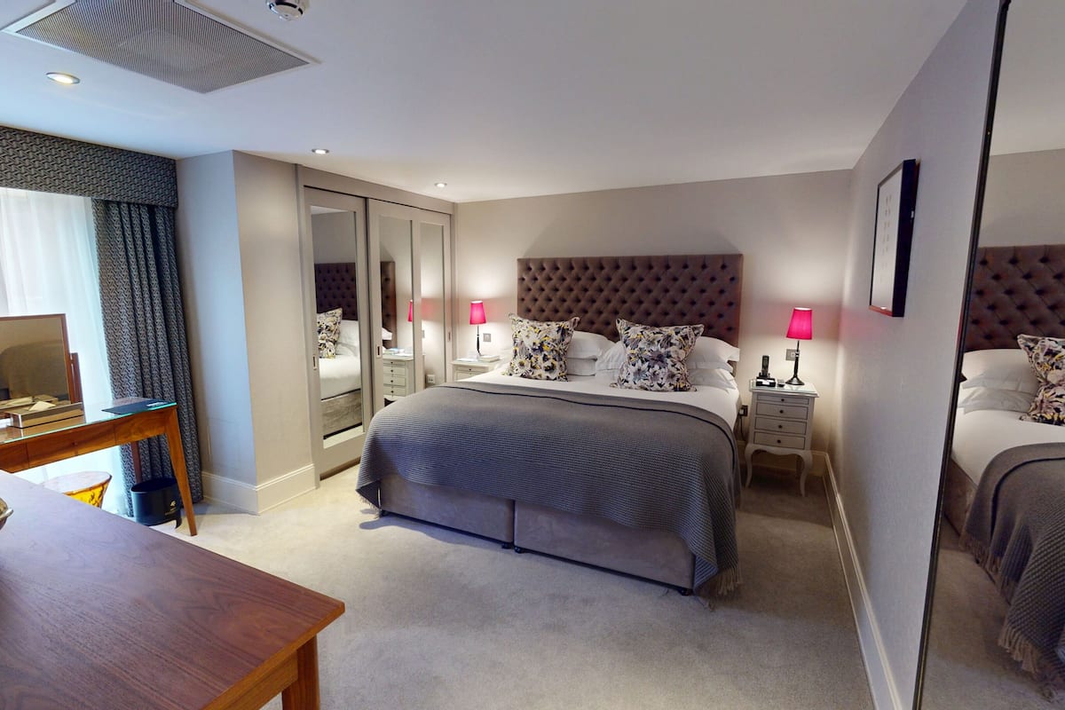 A modern hotel room with a large bed, a desk, a mirror, and a wardrobe.
