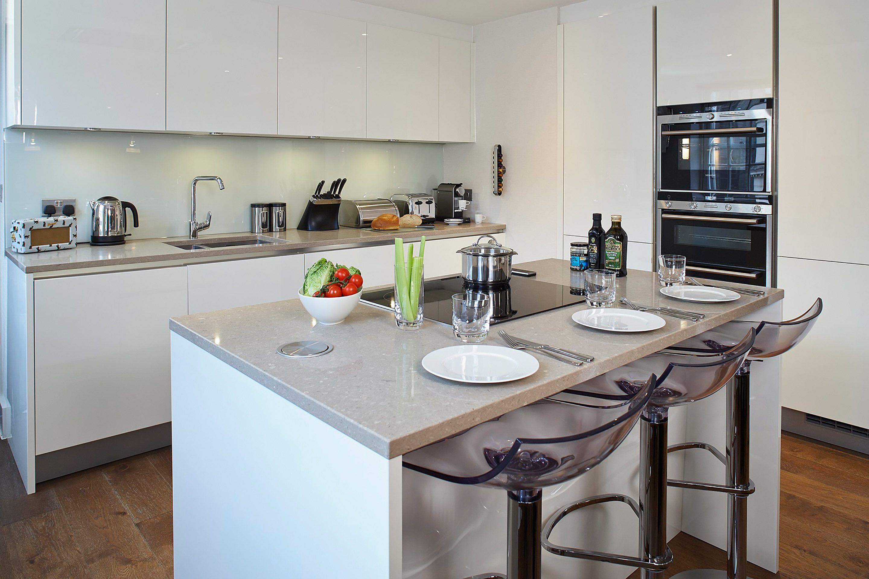 A modern kitchen with a central island, bar stools, a built-in oven, and a coffee machine.